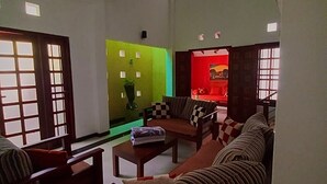 A spacious living room with a high ceiling, a green accent wall, and a red accent wall. There are two sofas, a coffee table, and a TV. - Luxury Villa Costanza (Hikkaduwa)
