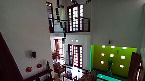 A spacious living area with a high ceiling, wooden beams, and a green accent wall. There is a staircase leading to an upper level, and the room is well-lit with natural light from windows. - Luxury Villa Costanza (Hikkaduwa)