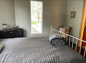 Une chambre à coucher avec un lit, une table de chevet, une lampe, une fenêtre et une porte.