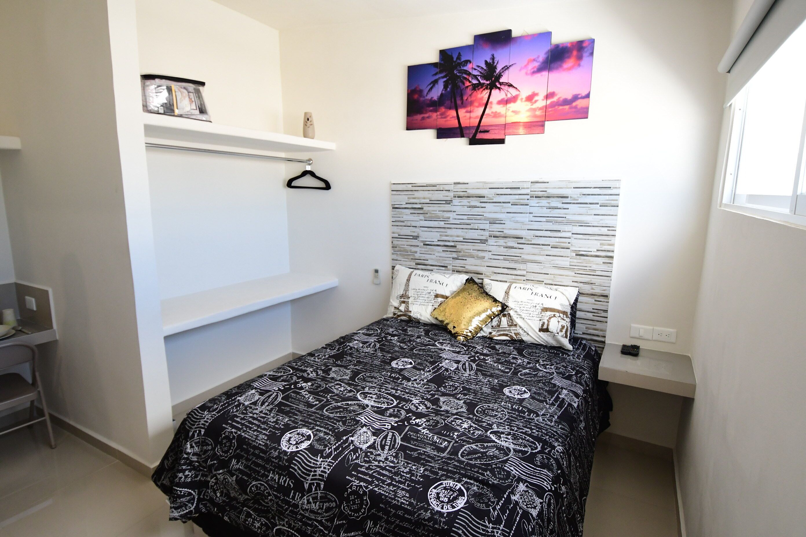 Ein Schlafzimmer mit einem Bett, einem Regal, einem Wandbild und einem Fenster.