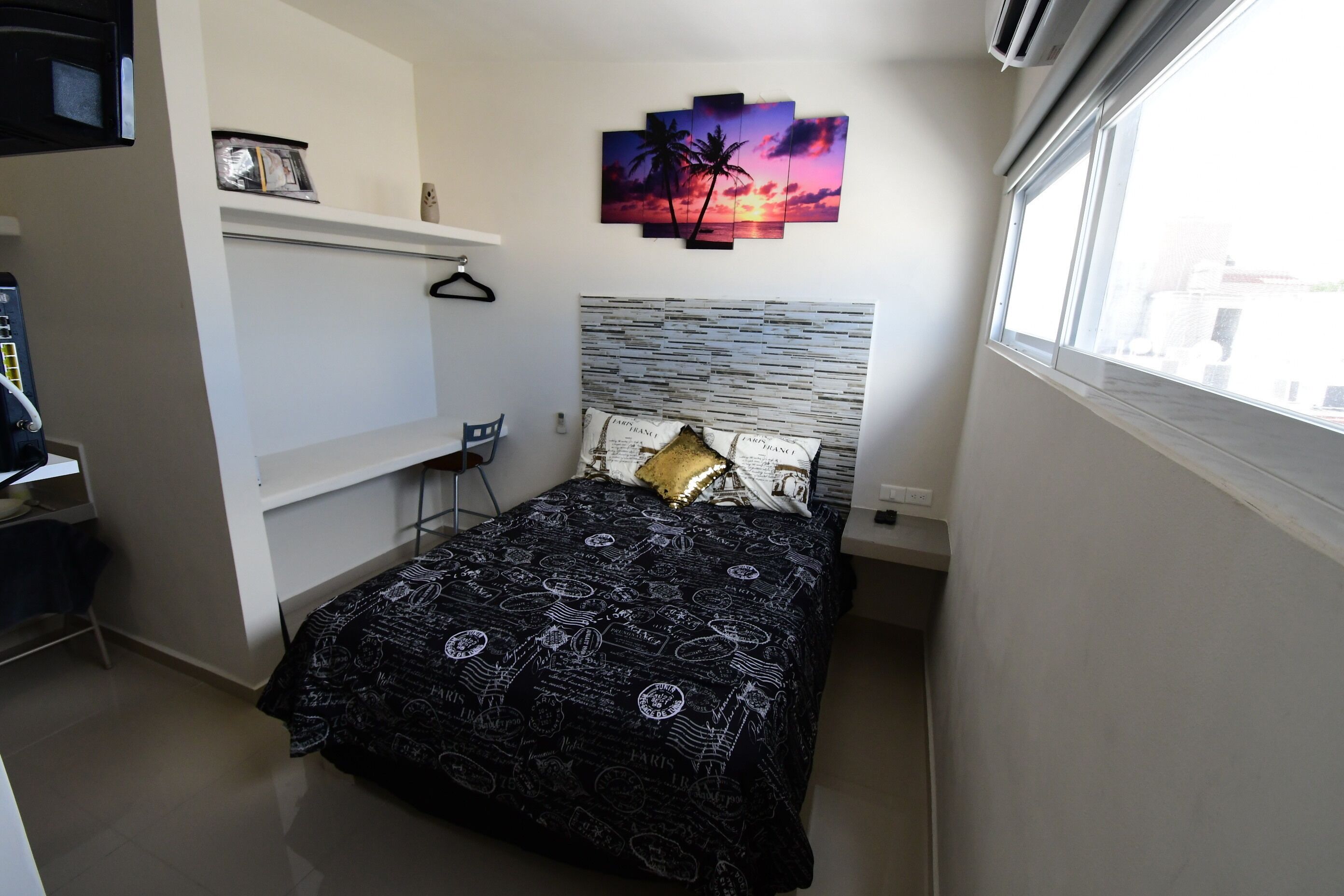 A bedroom with a bed, a desk, a chair, a shelf, and a window.