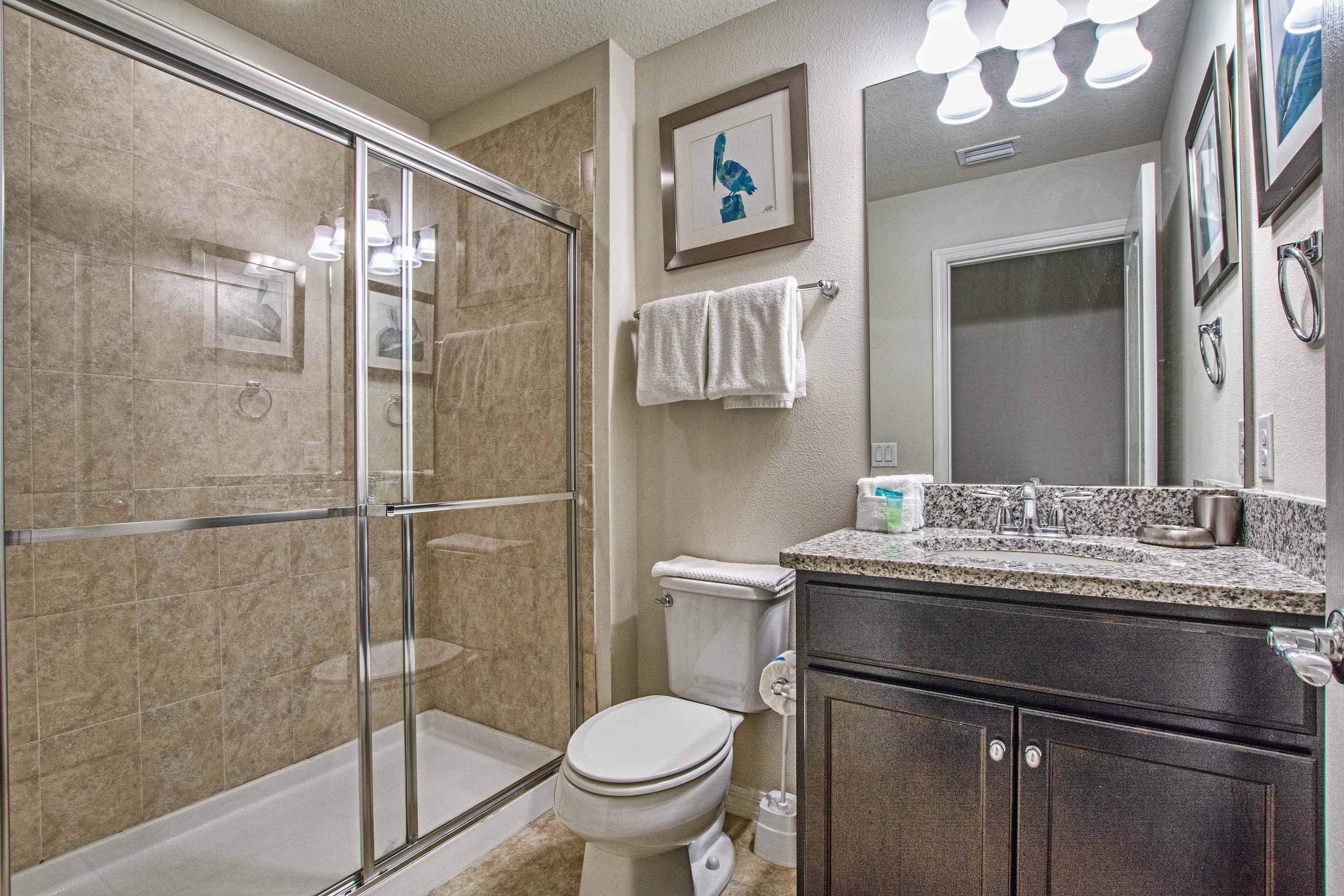 A bathroom with a glass-enclosed shower, a toilet, a sink with a granite countertop, and a mirror above the sink.