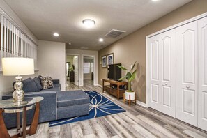 A living room with a sectional sofa, a coffee table, a TV on a stand, a potted plant, and a large wardrobe. - Windsor-5 Bed W/splashpool-3801ww 5 Bedroom Townhouse by RedAwning (Kissimmee)