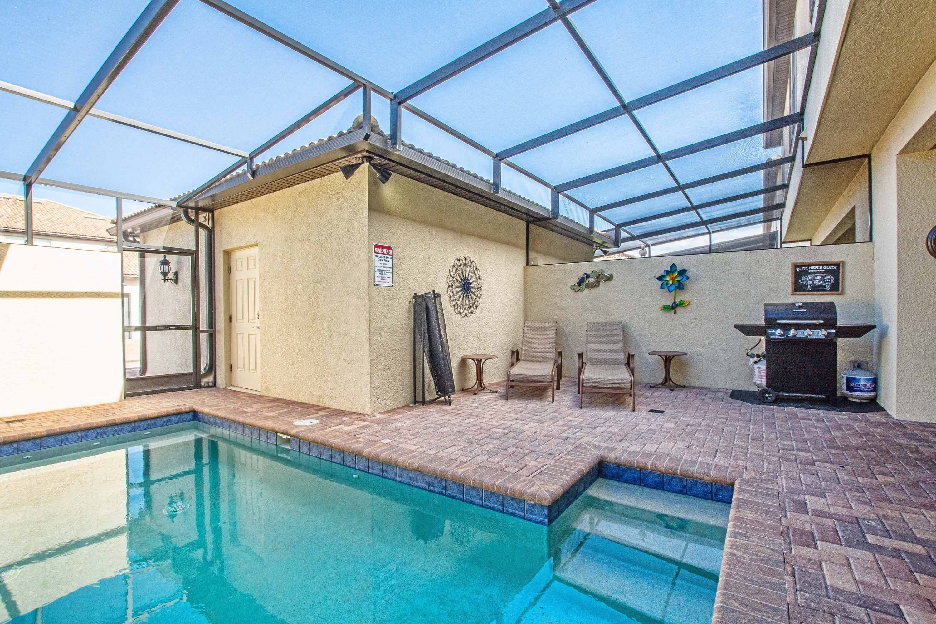 An indoor swimming pool with a glass ceiling, a barbecue grill, and a sign warning of hot water.