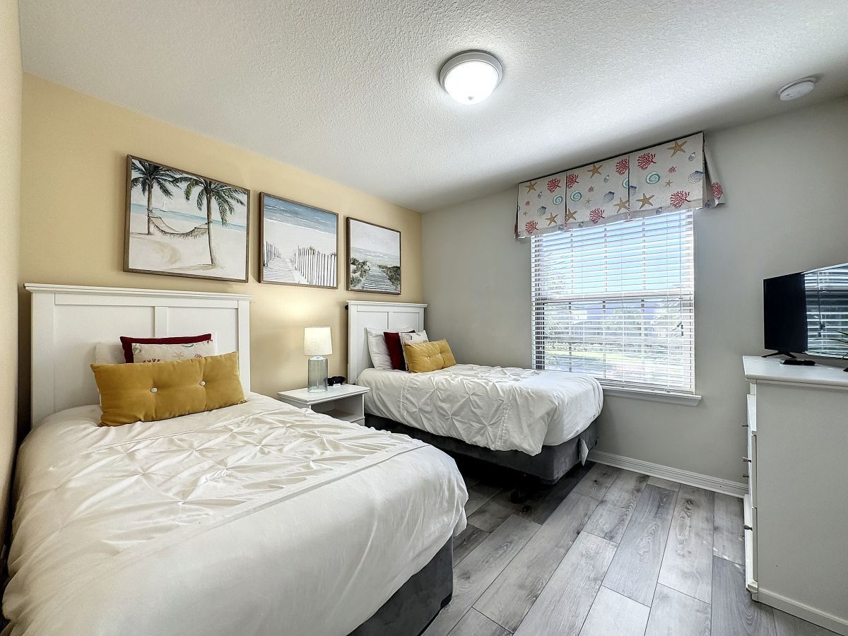 A hotel room with two beds, a nightstand, a desk, and a window with blinds.