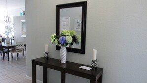 A console table with a vase of flowers and two candles, a mirror above it, and a dining area in the background.