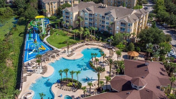 An aerial view of a resort with a large swimming pool, a water park, and multiple apartment buildings.