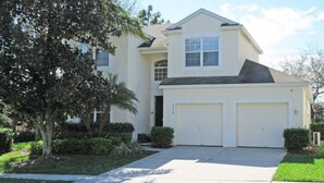 A two-story house with a garage, a front yard with a tree, and a clear sky.