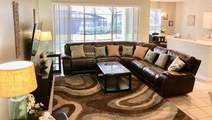 A living room with a brown leather sectional sofa, a glass coffee table, and a patterned rug.