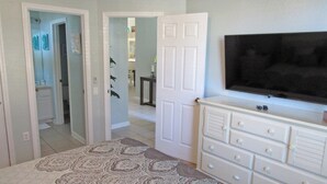 A bedroom with a bed, a dresser, a television, and a door leading to another room.