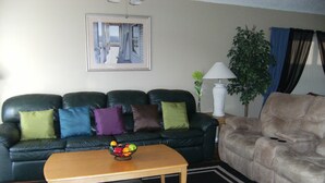 A living room with a black leather sofa, a beige armchair, a wooden coffee table with a fruit bowl, and a framed picture on the wall. - Prime Location In Secure Safe 247 Manned Gatehouse Community With Clubhouse (Kissimmee)