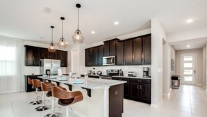 A modern kitchen with dark cabinets, a central island with bar stools, and pendant lighting. - South Facing With Lots Of Games In Game Room! 9 Bedroom Villa by RedAwning (Kissimmee)