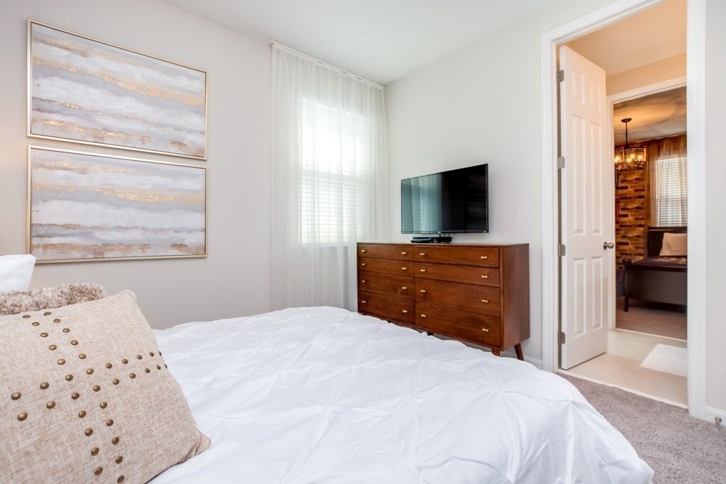 Quarto com uma cama, cómoda de madeira, televisão e porta para outro espaço.