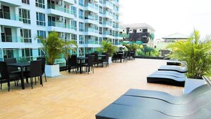 A rooftop lounge area with outdoor seating and tables, surrounded by a high-rise building with balconies. - The Cliff Pratumnak - Sea View Studio - Sleeps 2 (Pattaya)