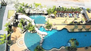 A swimming pool with multiple sections, surrounded by palm trees and lounge chairs. - The Cliff Pratumnak - Sea View Studio - Sleeps 2 (Pattaya)