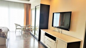 A hotel room with a bed, a TV mounted on the wall, a sliding glass door leading to a balcony, and a small seating area with chairs. - Beach Condo with Stunning Sea Views - Sleeps 2 (Pattaya)