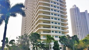 A high-rise building with multiple balconies, a swimming pool with lounge chairs, and palm trees. - Beach Condo with Stunning Sea Views - Sleeps 2 (Pattaya)