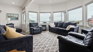 Ein geräumiges Wohnzimmer mit dunklen Sofas, einem gemusterten Teppich und großen Fenstern mit Blick.
