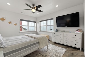 A bedroom with a bed, a dresser, a television, and windows.