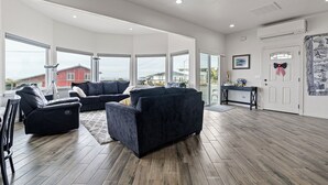 Ein geräumiges Wohnzimmer mit dunklen Sofas, einem Couchtisch und einem großen Fenster mit Blick auf ein rotes Gebäude.