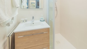 Ein modernes Badezimmer mit Duschabtrennung aus Glas, einem weißen Waschbecken mit Spiegel darüber und einer Holdeinrichtung mit Schubladen.