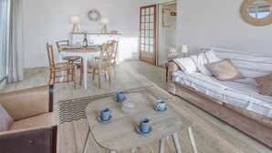 En hyggelig stue med sofa, sofabord med kopper, spiseplads med stole og bord, og en dør der fører til et andet rum.