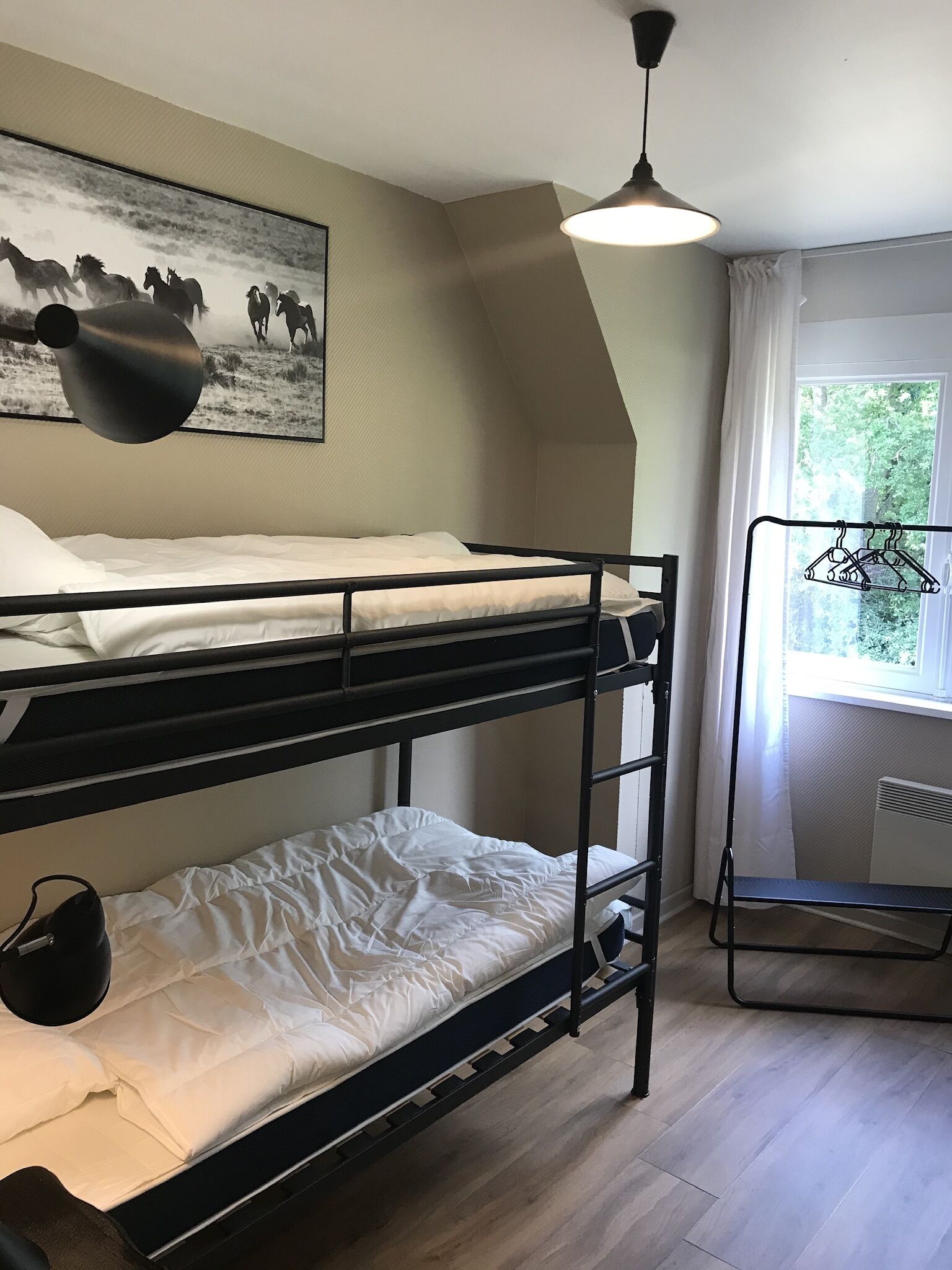 Habitación con literas, ventilador de techo, ventana con vista a follaje y un cuadro de caballos colgado en la pared.