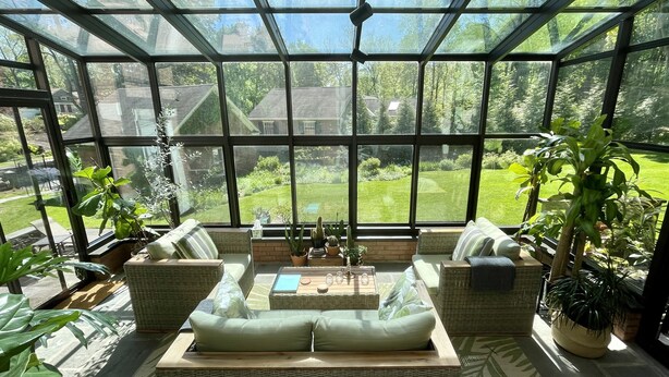 Un invernadero con muebles de mimbre, plantas en macetas y vistas a un jardín verde.