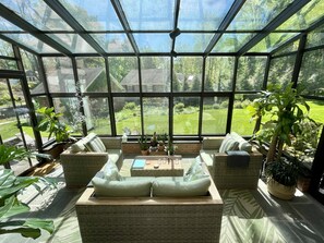 Un invernadero con muebles de mimbre, plantas en macetas y vistas a un césped verde.