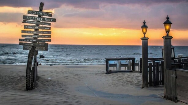 Una playa con un cartel de madera, una valla de madera y un farol.