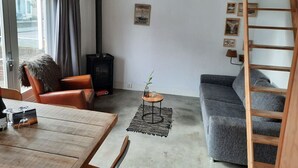 Una sala de estar acogedora con un sofá, una silla, una mesa de madera, una mesita auxiliar, una chimenea y una cama en un altillo.