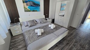 Une chambre à coucher moderne, dotée d’un grand lit, d’une table de chevet, d’une armoire et d’un tableau représentant un paysage côtier.