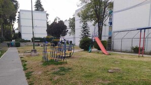 Ein Spielplatz mit Schaukeln und Rutsche, umgeben von Gras und Bäumen.