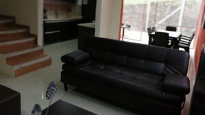 Uma sala de estar moderna com um sofá de couro preto, uma mesa de centro e uma escada que dá para uma cozinha.
