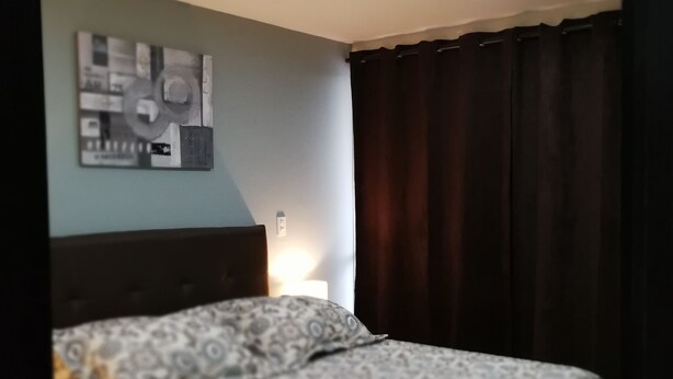 Quarto com cama, uma obra de arte na parede, abajur e cortinas escuras.
