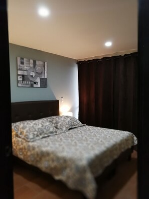 A bedroom with a bed, a wall-mounted artwork, a bedside lamp, and dark curtains. - New and Cozy House in the Heart of the Coffee Region (Pereira)