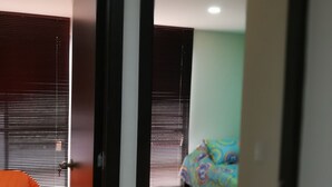 Vista interna de um quarto com uma cama, uma porta e uma janela com persianas.
