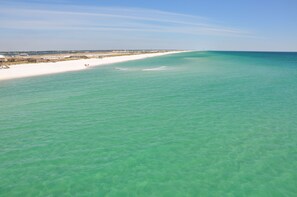 A beach with clear turquoise water, a sandy shore, and a pier in the distance. - Beach Bliss Stylish Pet Friendly Home Gulf View w/ Loft + Decks (Navarre)