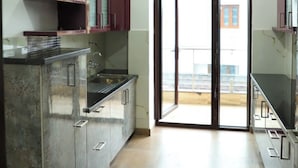 A kitchen with a central island, cabinets, and a sliding glass door leading to a balcony. - Excellent Property With Exellent Amenities You Would Love To Live In (Rishikesh)