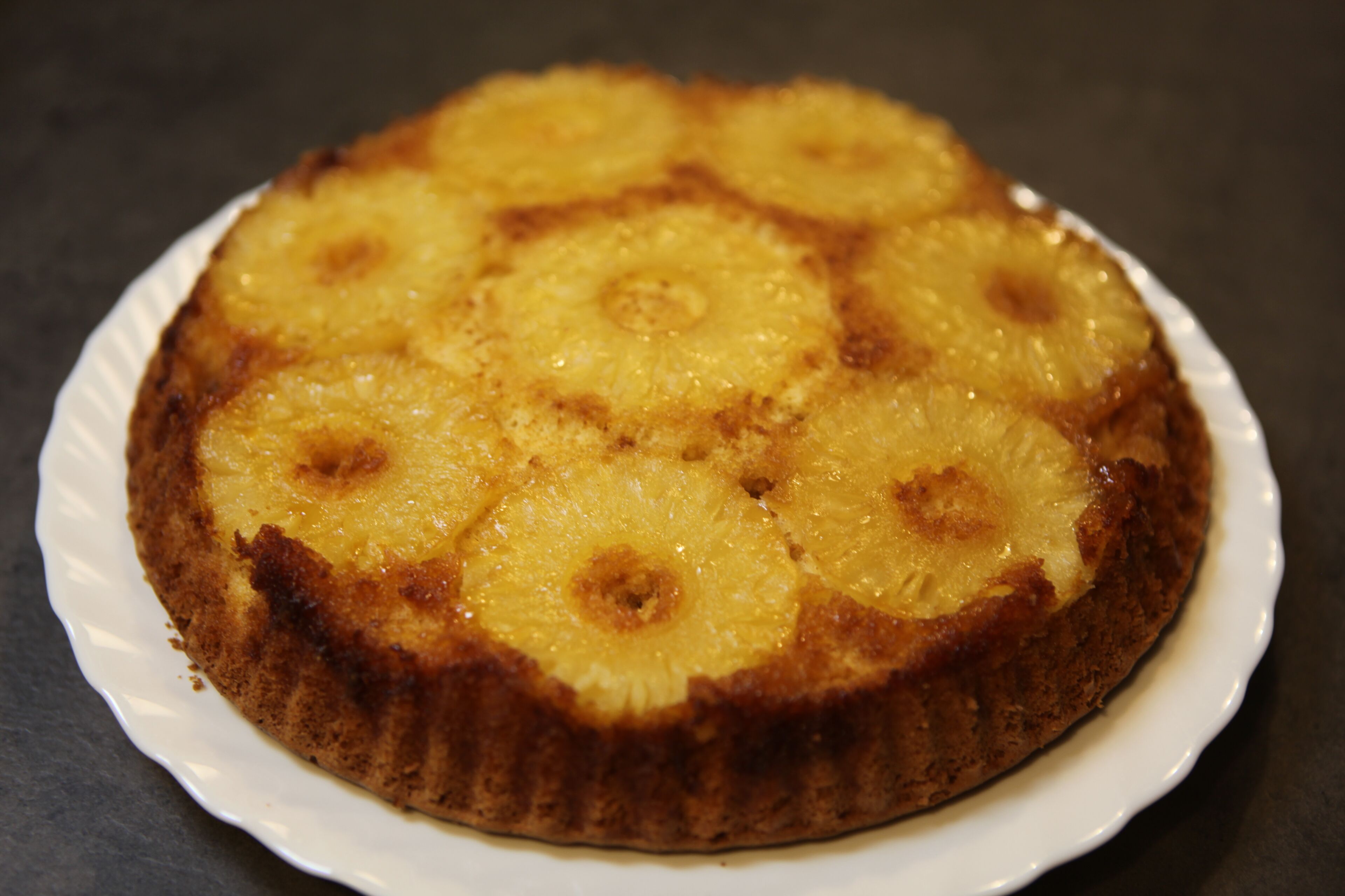 Un pastel redondo con rodajas de piña encima, sobre un plato blanco.