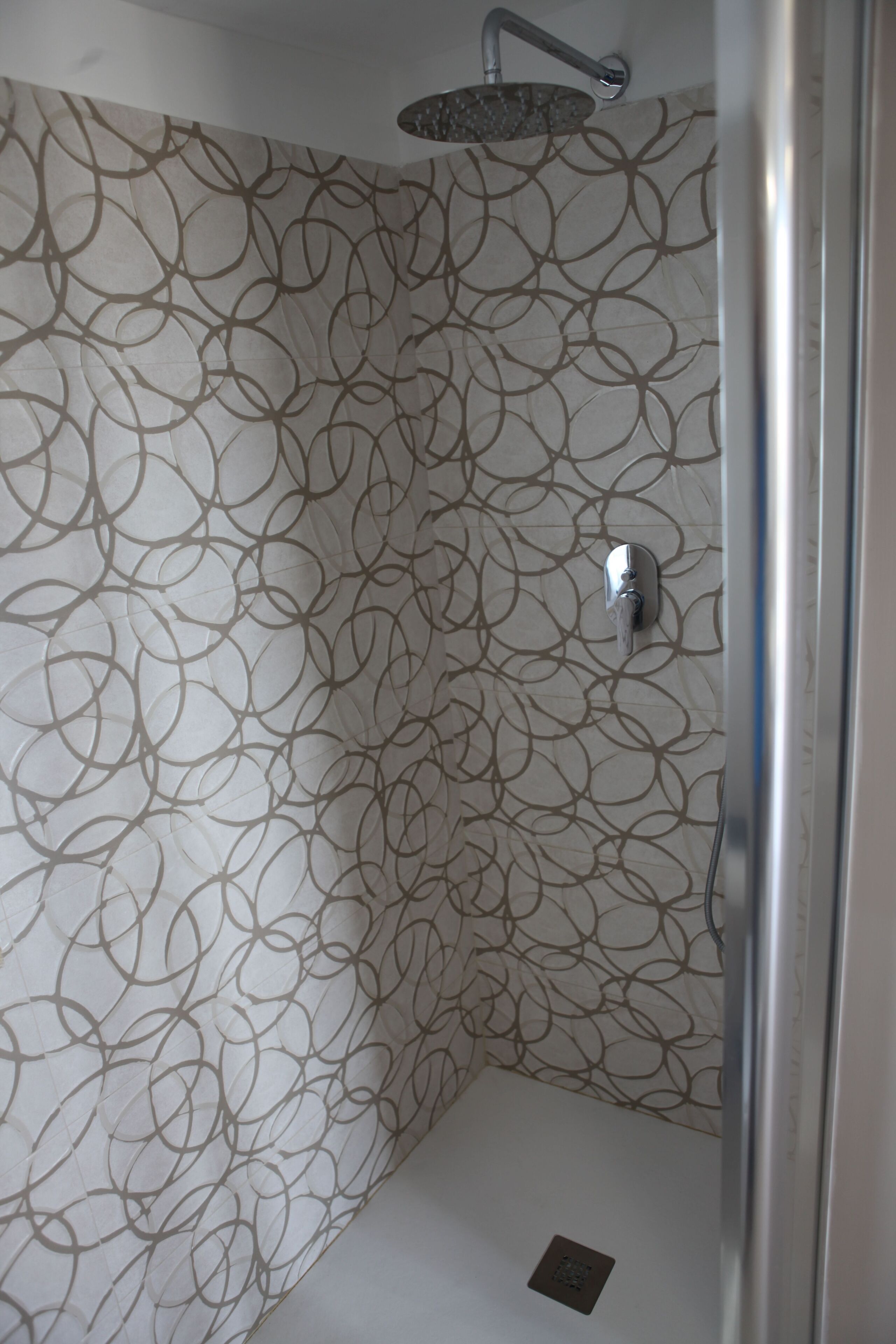 A shower with a circular pattern on the wall, a showerhead, and a drain.