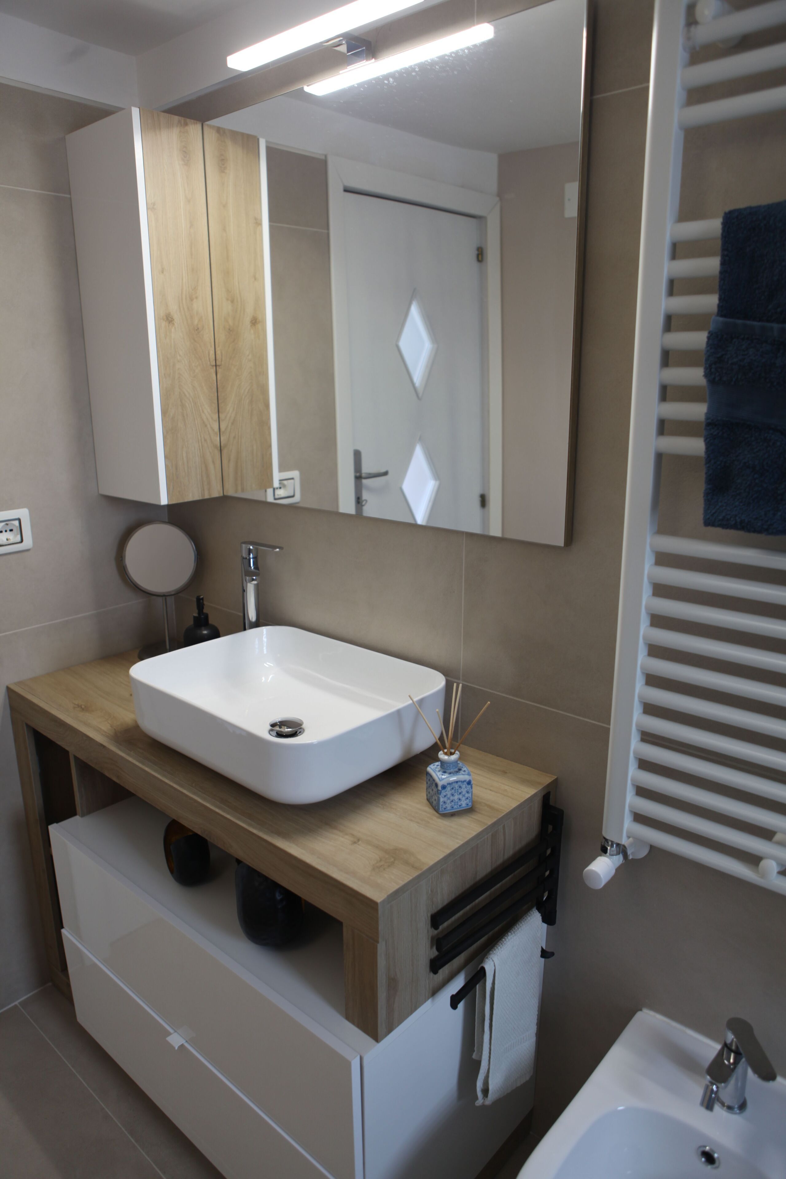 A modern bathroom with a wooden vanity, a white sink, a mirror, and a towel rack.