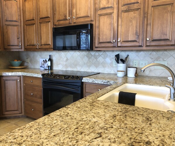 Una cocina con armarios de madera, microondas de acero inoxidable, estufa negra, encimeras de granito, un fregadero y una cafetera.
