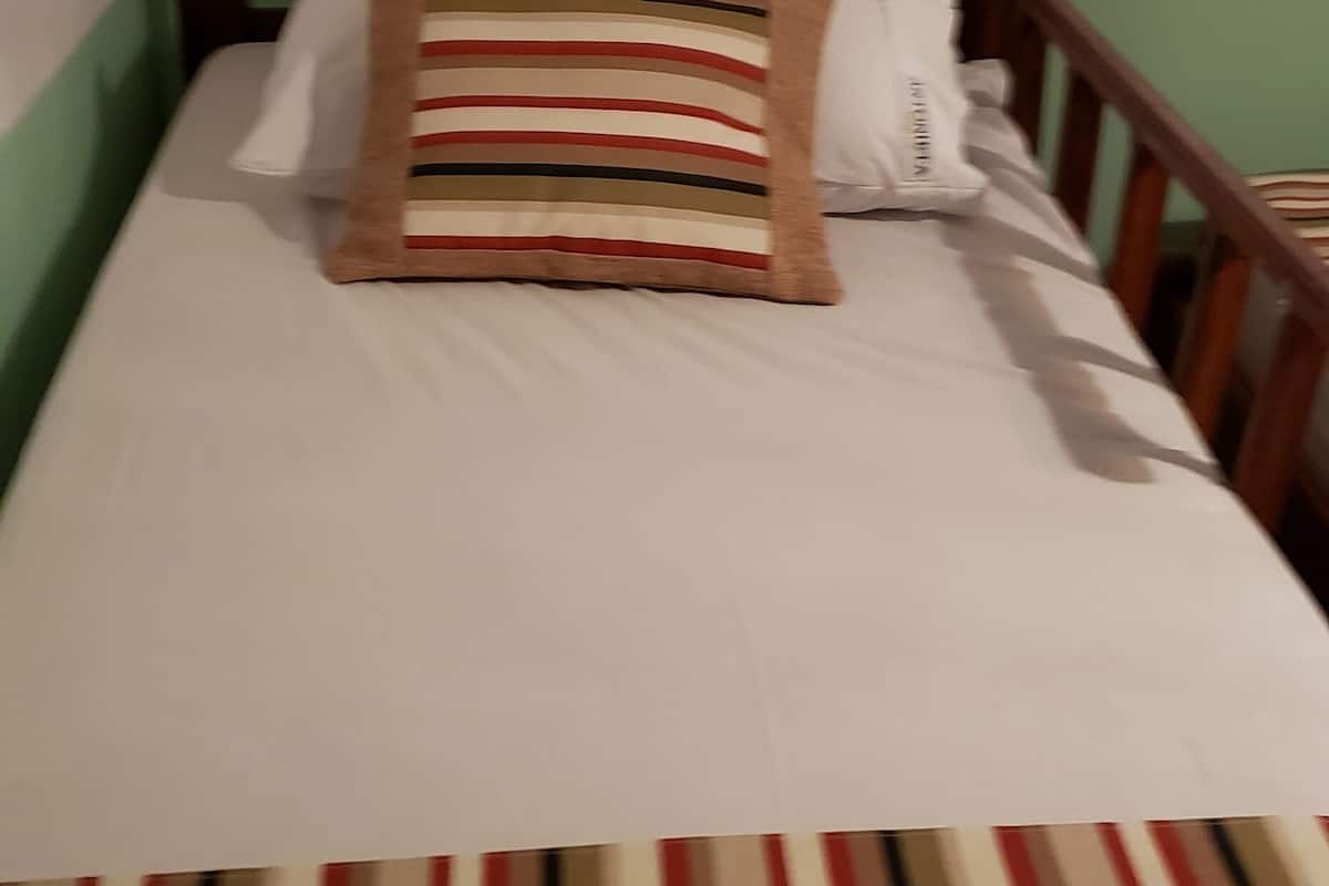 Ein Bett mit gestreifter Bettdecke, einem Holz-Kopfteil und zwei Kissen, eines gestreift und eines einfarbig.