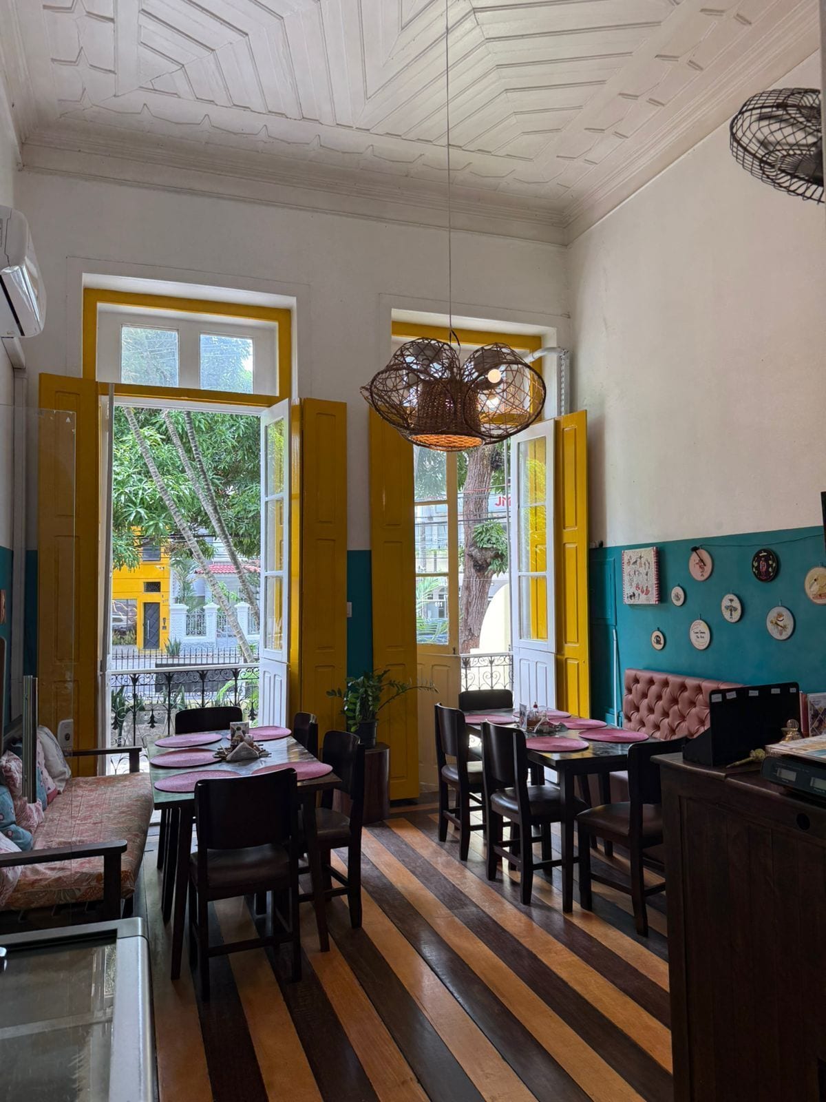 Un comedor con piso de madera a rayas, puertas amarillas y una lámpara colgante de fibra.