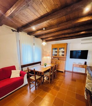 A cozy living room with a red sofa, wooden dining table, and a TV mounted on the wall. - Quiet and Relaxing, Surrounded by Greenery a few Kilometers From the sea (Sarroch)