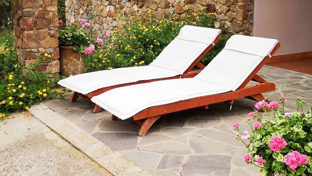 Two wooden lounge chairs with white cushions, positioned on a stone patio with a stone wall and a window with wooden shutters in the background. - Quiet and Relaxing, Surrounded by Greenery a few Kilometers From the sea (Sarroch)