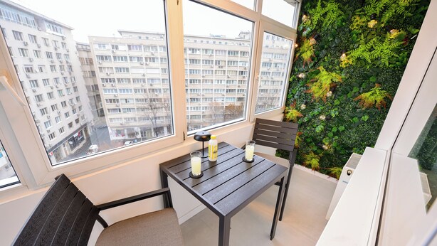 Un balcon avec une table et des chaises, une vue sur les immeubles et un mur végétal.