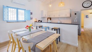 Una cocina moderna con armarios blancos, un refrigerador empotrado y un comedor con mesa de vidrio y sillas de madera.