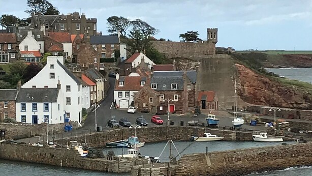 A coastal town with historic buildings, a castle, and a harbor with boats.